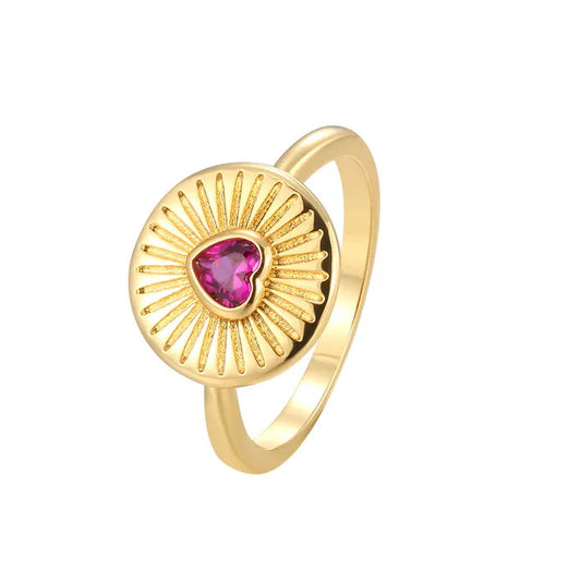Bague dorée en forme de médaillon solaire avec un cœur rose fuchsia facetté, symbole lumineux mêlant chaleur du doré et éclat de la pierre.