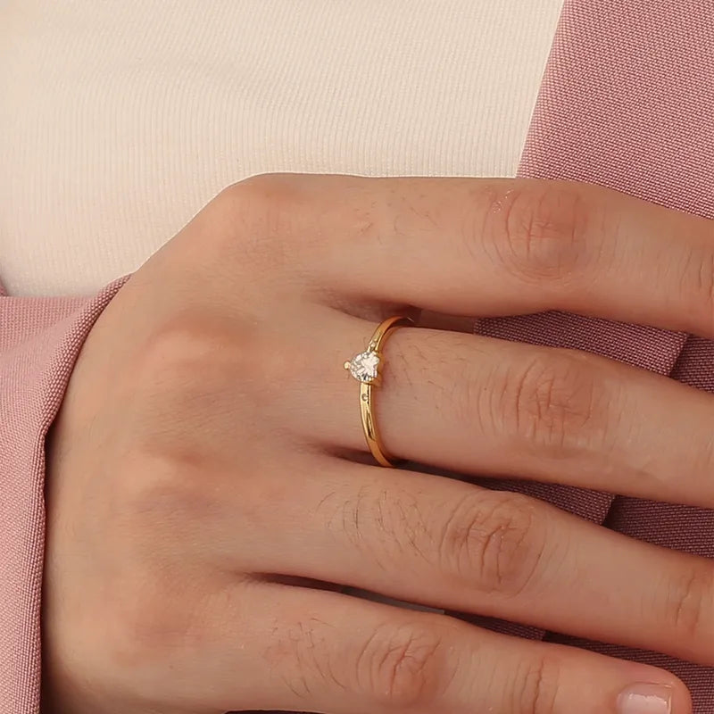 Bague dorée or 18K pour femme, ornée d’un zircon blanc en forme de cœur accompagné de deux pierres latérales scintillantes, au style romantique, minimaliste et raffiné, parfaite comme bague de promesse ou cadeau d’amour.