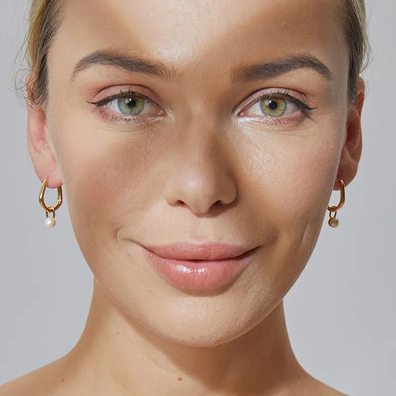 Boucles d’oreilles créoles dorées asymétriques pour femme en plaqué or, ornées d’une perle blanche pendante. Bijou chic et minimaliste au design fluide et moderne, alliant élégance intemporelle et raffinement contemporain