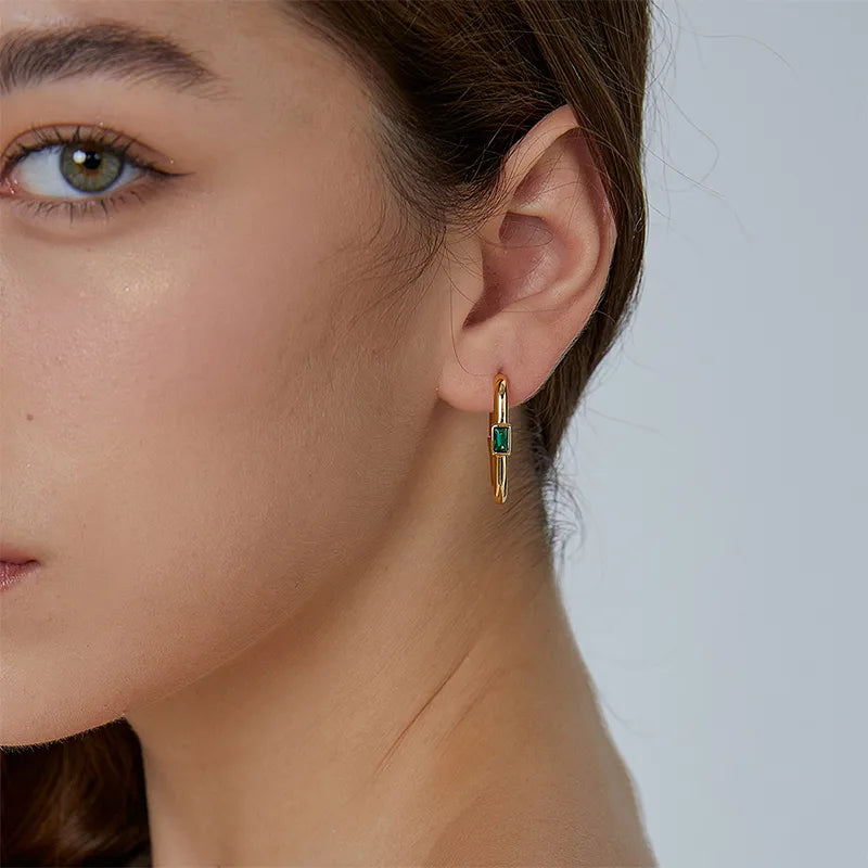 Boucles d’oreilles créoles rectangulaires dorées pour femme en plaqué or, ornées d’un zircon vert taillé en baguette au centre. Bijou géométrique et contemporain au design structuré et raffiné, idéal pour un look moderne et urbain