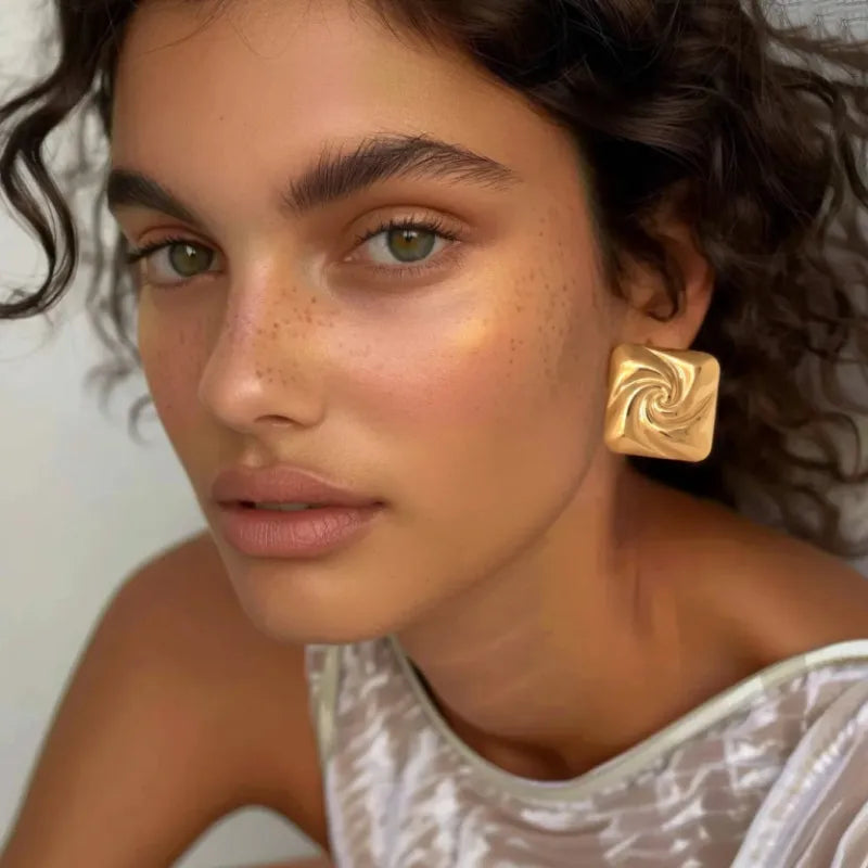 Paire de boucles d’oreilles dorées carrées en acier inoxydable, au design spiralé brillant et à l’effet miroir, parfaites pour un look chic et contemporain.