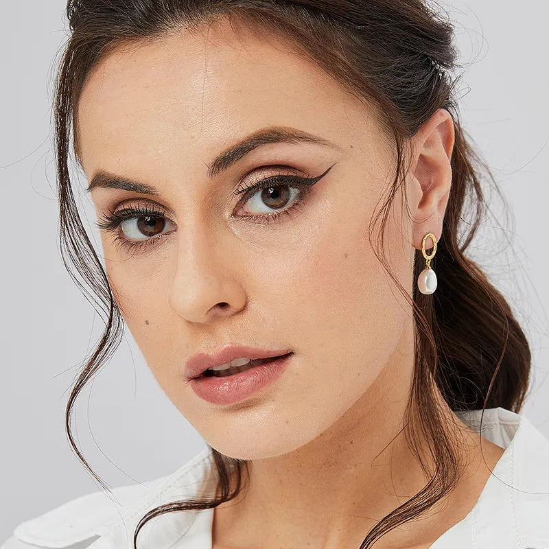 Boucles d’oreilles pendantes dorées pour femme, composées d’un ovale martelé doré et d’une perle blanche baroque suspendue. Bijou au style bohème chic et raffiné, lumineux et féminin, parfait pour sublimer une tenue naturelle ou romantique