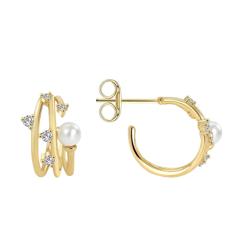 Boucles d’oreilles puces dorées pour femme en plaqué or, composées de deux anneaux entrelacés ornés de zircons scintillants et d’une perle blanche ronde. Bijou chic et raffiné, au design moderne et féminin, idéal pour une tenue habillée ou élégante au quotidien