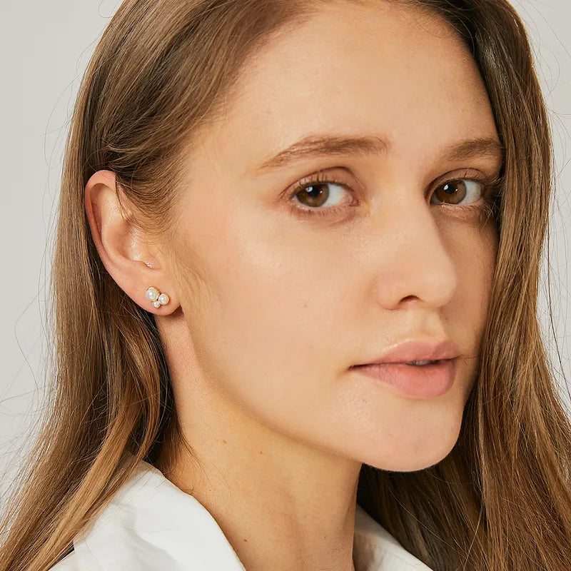 Boucles d’oreilles puces dorées pour femme en plaqué or, ornées de trois perles blanches disposées en grappe minimaliste. Bijou délicat et lumineux au style chic et féminin, parfait pour un look minimaliste ou une accumulation raffinée.