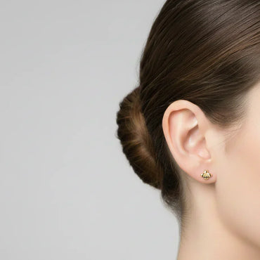 Oreille féminine avec boucle d'oreille abeille en or sur fond gris clair