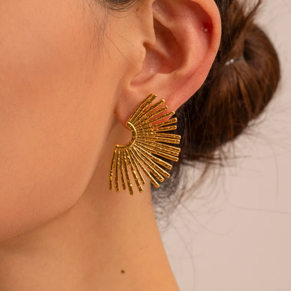 Des boucles d’oreilles puces au design solaire, puissantes et expressives, inspirées d’un éventail de lumière. Leur forme évoque à la fois des ailes déployées et un coucher de soleil stylisé, pour un rendu résolument moderne et sculptural.

Matériau : Acier inoxydable couleur doré, résistant à l’eau, sans ternissure, hypoallergénique.

Dimensions : 44 x 26 mm – format large, affirmé, mais léger (12 g la paire).

Design : Structure en éventail rayonnant, effet martelé subtil qui capte la lumière. Style graph