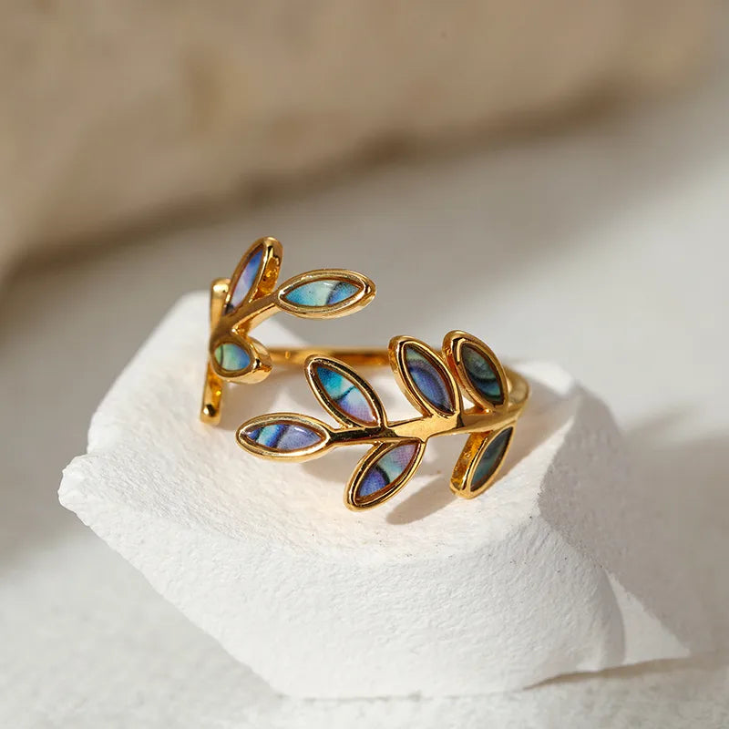 Apportez une touche d’élégance naturelle à votre style avec cette bague en acier inoxydable doré, ornée de délicates feuilles incrustées de coquille d’ormeau. Son design ouvert épouse parfaitement la forme du doigt tout en reflétant la lumière avec subtilité grâce aux reflets irisés de la nacre.