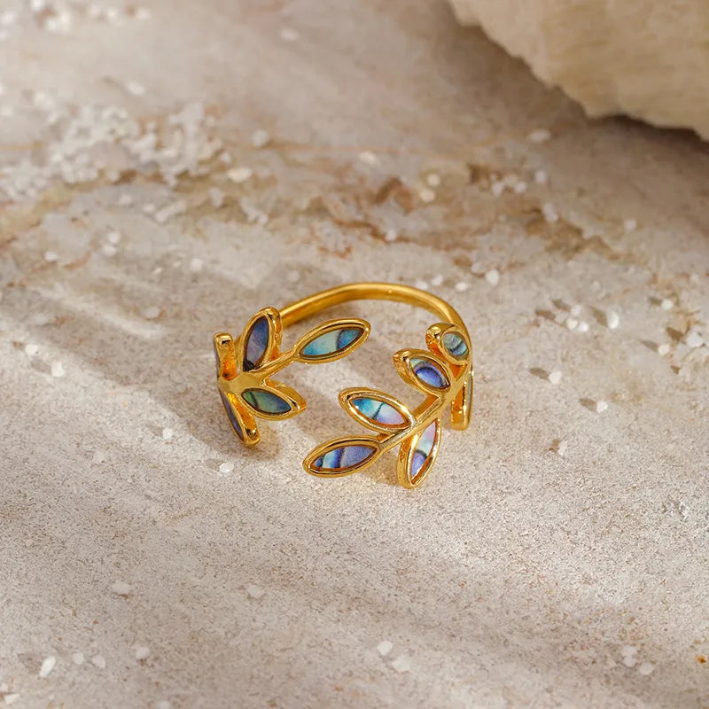 Apportez une touche d’élégance naturelle à votre style avec cette bague en acier inoxydable doré, ornée de délicates feuilles incrustées de coquille d’ormeau. Son design ouvert épouse parfaitement la forme du doigt tout en reflétant la lumière avec subtilité grâce aux reflets irisés de la nacre.