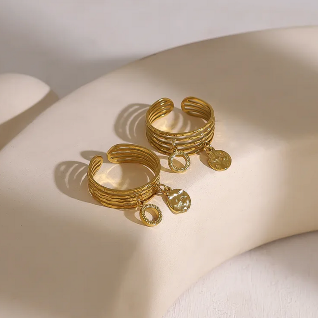Bague dorée multi-rangs à l’allure bohème chic, ornée de deux breloques martelées qui ajoutent mouvement et éclat à votre main. L’alternance de lignes texturées donne un effet à la fois brut et raffiné, parfait pour un style affirmé et libre.

Réalisée en acier inoxydable avec un placage PVD or 18K, cette bague est résistante à l’eau, anti-ternissure et hypoallergénique. Un bijou fait pour durer, à porter au quotidien sans souci.

Matériaux : Acier inoxydable avec placage PVD or 18K, breloques texturées
Dim