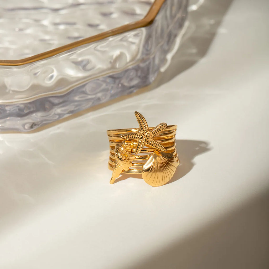 Ajoutez une touche marine et audacieuse à votre style avec cette bague dorée à l’or fin inspirée de l’univers marin. Ornée d’un trio de charms détaillés – une étoile de mer, un coquillage et un corail stylisé – elle incarne l’esprit des vacances avec élégance et originalité.