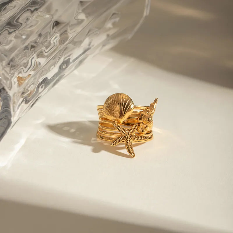 Ajoutez une touche marine et audacieuse à votre style avec cette bague dorée à l’or fin inspirée de l’univers marin. Ornée d’un trio de charms détaillés – une étoile de mer, un coquillage et un corail stylisé – elle incarne l’esprit des vacances avec élégance et originalité.