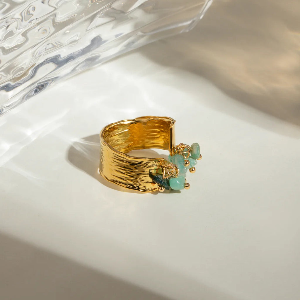 Ajoutez une touche de caractère et de fraîcheur à votre style avec cette bague ajustable en acier inoxydable doré ornée de pierres naturelles vert d’eau. Son design martelé associé à des pendentifs de pierres semi-précieuses crée un jeu de texture et de lumière unique, pour un bijou aussi audacieux qu’élégant.