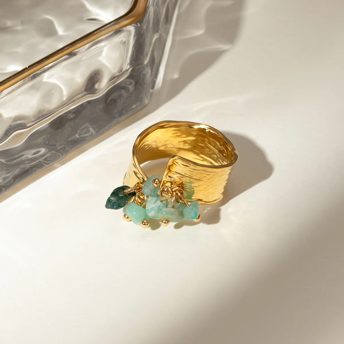 Ajoutez une touche de caractère et de fraîcheur à votre style avec cette bague ajustable en acier inoxydable doré ornée de pierres naturelles vert d’eau. Son design martelé associé à des pendentifs de pierres semi-précieuses crée un jeu de texture et de lumière unique, pour un bijou aussi audacieux qu’élégant.