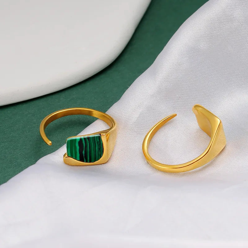 Ajoutez une touche d'audace à votre collection avec cette bague en acier inoxydable doré ornée d’un éclatant fragment de malachite naturelle. Son design ouvert et contemporain s’allie parfaitement à l’élégance de la pierre verte, connue pour ses magnifiques stries noires et vertes uniques.