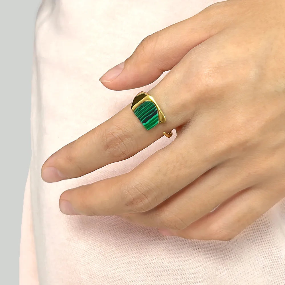 Ajoutez une touche d'audace à votre collection avec cette bague en acier inoxydable doré ornée d’un éclatant fragment de malachite naturelle. Son design ouvert et contemporain s’allie parfaitement à l’élégance de la pierre verte, connue pour ses magnifiques stries noires et vertes uniques.