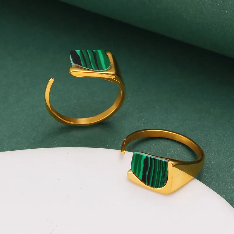 Ajoutez une touche d'audace à votre collection avec cette bague en acier inoxydable doré ornée d’un éclatant fragment de malachite naturelle. Son design ouvert et contemporain s’allie parfaitement à l’élégance de la pierre verte, connue pour ses magnifiques stries noires et vertes uniques.