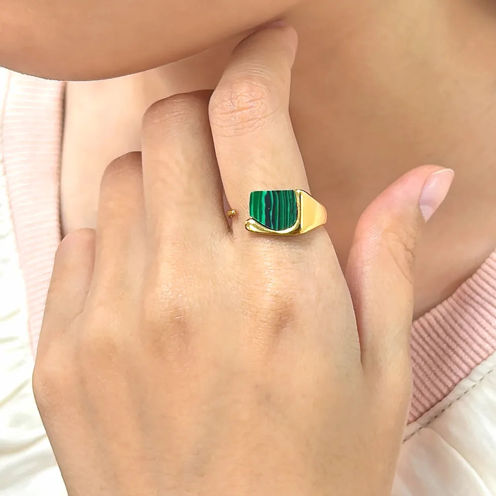 Ajoutez une touche d'audace à votre collection avec cette bague en acier inoxydable doré ornée d’un éclatant fragment de malachite naturelle. Son design ouvert et contemporain s’allie parfaitement à l’élégance de la pierre verte, connue pour ses magnifiques stries noires et vertes uniques.