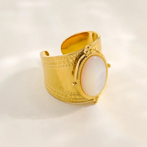 Faites sensation avec cette bague dorée large, sublimée par une pierre blanche ovale nacrée et des détails finement gravés. Son design audacieux s’inspire des bijoux d’influence antique, pour une allure royale et contemporaine à la fois.