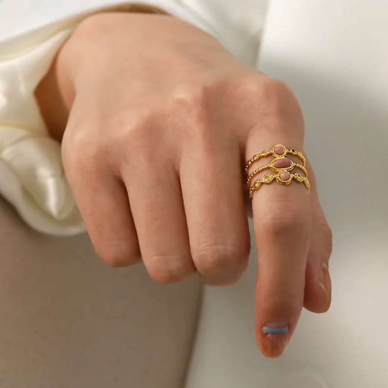 Craquez pour l’élégance de cette bague dorée à effet triple anneau, délicatement sertie de trois pierres roses aux reflets nacrés. Sa structure perlée et ajourée lui confère un charme rétro et romantique, parfait pour sublimer vos tenues avec une touche poétique et raffinée.