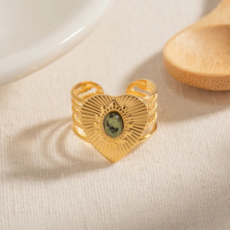 Rayonnez avec cette bague en forme de cœur doré, finement gravée de rayons texturés autour d’un cabochon pierre verte. Ce bijou à l’allure solaire et protectrice mêle symbolisme spirituel et design affirmé, parfait pour révéler votre lumière intérieure.