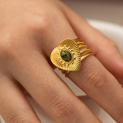 Rayonnez avec cette bague en forme de cœur doré, finement gravée de rayons texturés autour d’un cabochon pierre verte. Ce bijou à l’allure solaire et protectrice mêle symbolisme spirituel et design affirmé, parfait pour révéler votre lumière intérieure.