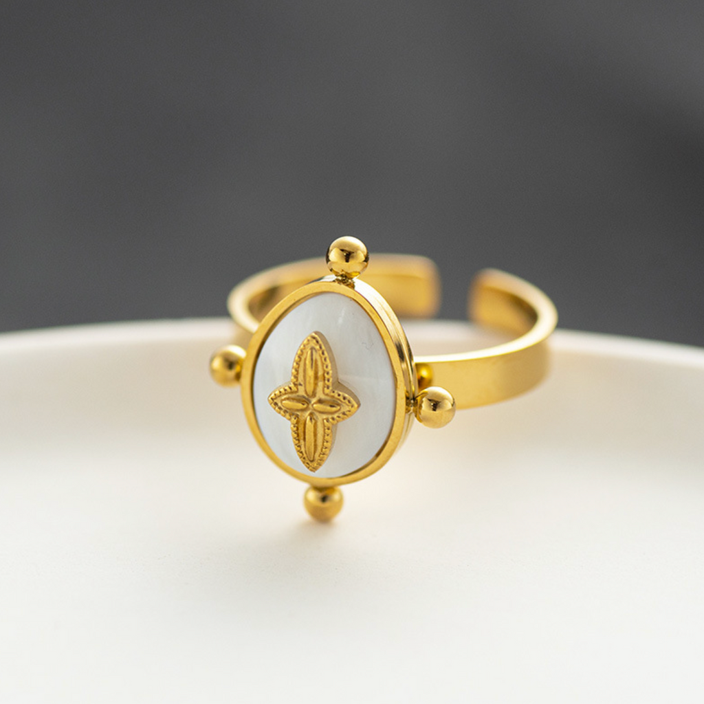 Une bague au design doux et raffiné, où une fleur en relief se pose délicatement sur un fond nacré lumineux, encadré de perles dorées symboliques. Un bijou qui allie féminité et élégance dans un esprit poétique.

Matériau : Acier inoxydable couleur doré, rehaussé d’une pastille en nacre synthétique, finitions lisses et brillantes. Résistante à l’eau, hypoallergénique, conçue pour durer.

Dimensions : Anneau ajustable, large et confortable. Plateau central ovale orné d’une fleur stylisée à quatre pétales, bo