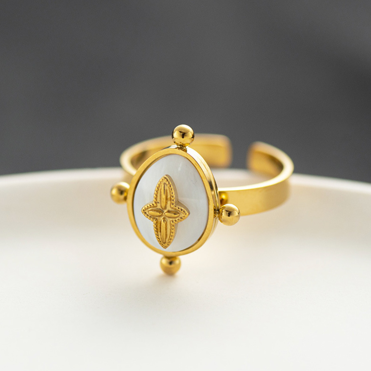 Une bague au design doux et raffiné, où une fleur en relief se pose délicatement sur un fond nacré lumineux, encadré de perles dorées symboliques. Un bijou qui allie féminité et élégance dans un esprit poétique.

Matériau : Acier inoxydable couleur doré, rehaussé d’une pastille en nacre synthétique, finitions lisses et brillantes. Résistante à l’eau, hypoallergénique, conçue pour durer.

Dimensions : Anneau ajustable, large et confortable. Plateau central ovale orné d’une fleur stylisée à quatre pétales, bo
