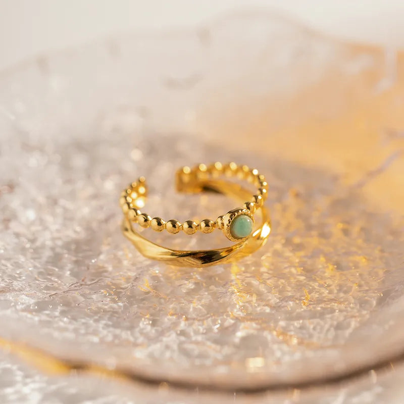 Offrez une touche de douceur minérale à votre main avec cette bague dorée en acier inoxydable, combinant un anneau perlé délicat et une bague torsadée lisse, unies par une pierre amazonite centrale aux reflets verts apaisants. Un bijou chic, fin et symbolique à la fois.