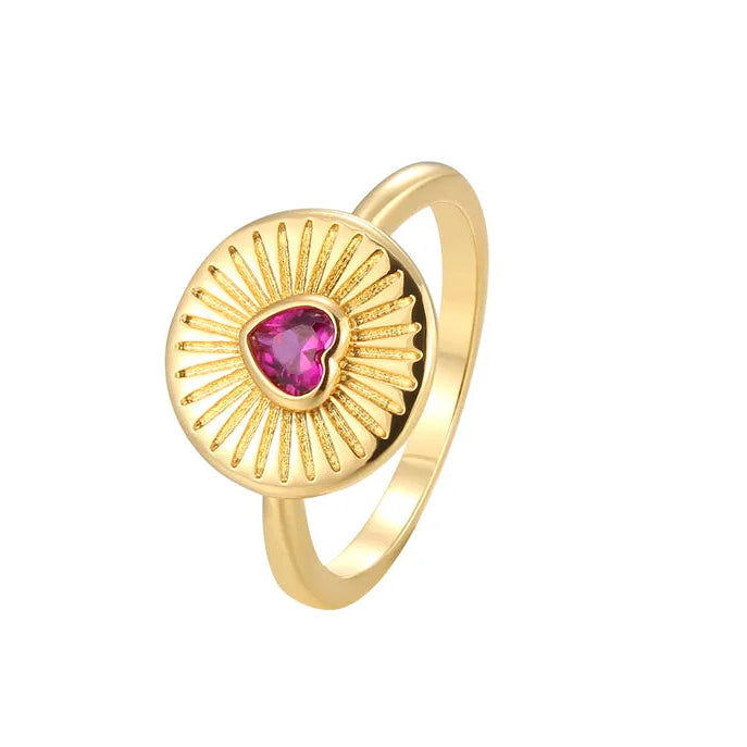 Bague dorée en forme de médaillon solaire avec un cœur rose fuchsia facetté, symbole lumineux mêlant chaleur du doré et éclat de la pierre.