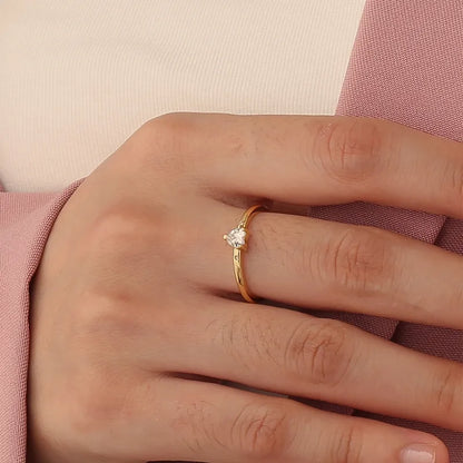 Bague dorée or 18K pour femme, ornée d’un zircon blanc en forme de cœur accompagné de deux pierres latérales scintillantes, au style romantique, minimaliste et raffiné, parfaite comme bague de promesse ou cadeau d’amour.