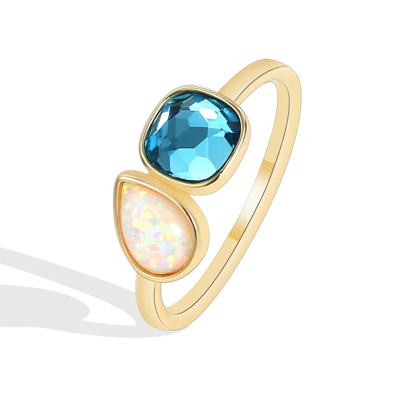 Bague dorée or 18K pour femme, ornée de deux pierres asymétriques – une bleue facettée et une blanche effet opale –, au design moderne et lumineux, parfaite pour un style estival, créatif et élégant.
