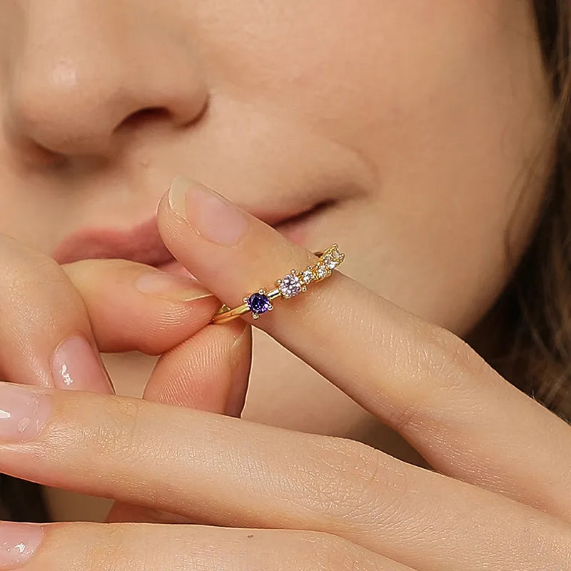 Bague dorée or 18K pour femme, ornée de zircons colorés bleu saphir, rose poudré et blancs alignés sur une ligne fine incurvée, au style minimaliste, coloré et féminin, parfaite pour ajouter une touche lumineuse et raffinée.