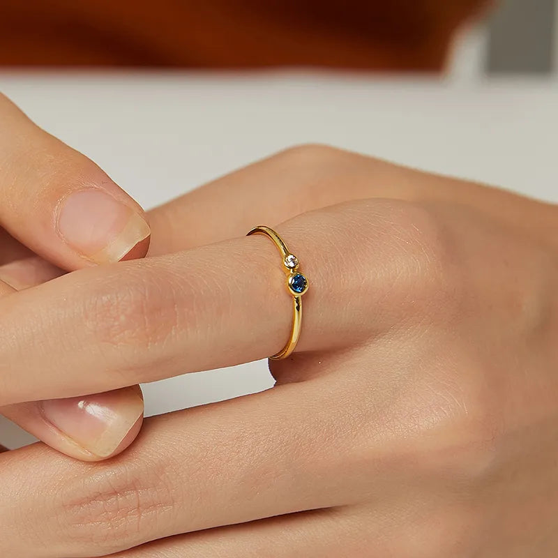 Inspirée de l’équilibre et de la pureté, cette bague dorée fine arbore un duo de pierres rondes : une pierre bleu nuit au halo mystérieux et un zircon blanc étincelant, comme deux astres alignés. Leur position légèrement décentrée renforce le caractère moderne et graphique de ce bijou.