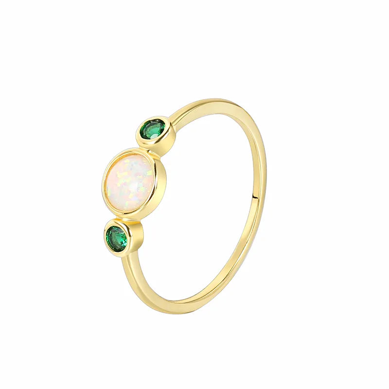 Bague fine plaqué or avec opale blanche irisée au centre et deux zircons verts profonds, au design minimaliste et équilibré, offrant une élégance naturelle et lumineuse.