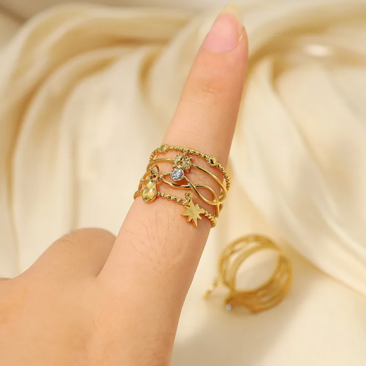 Bague fantaisie dorée à l’allure céleste, composée de plusieurs rangs texturés entrelacés, ponctués de breloques étoiles, cristaux scintillants et détails perlés. Une pièce forte et ludique qui attire immédiatement le regard avec son effet de superposition maîtrisé.

Conçue en acier inoxydable couleur doré, finition PVD or 18K, elle est résistante à l’eau, hypoallergénique et durable dans le temps. Un bijou à porter sans contrainte.

Matériaux : Acier inoxydable doré – Cristal – Placage PVD or 18K
Dimension