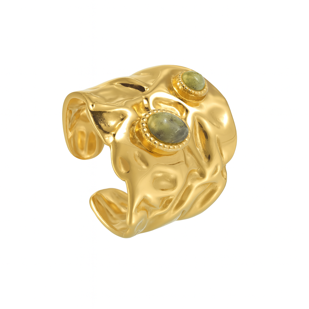 cette bague large dorée en acier inoxydable, au design martelé façon métal fondu. Deux pierres naturelles vertes en cabochon viennent illuminer sa structure organique, pour un effet à la fois mystique et résolument moderne.