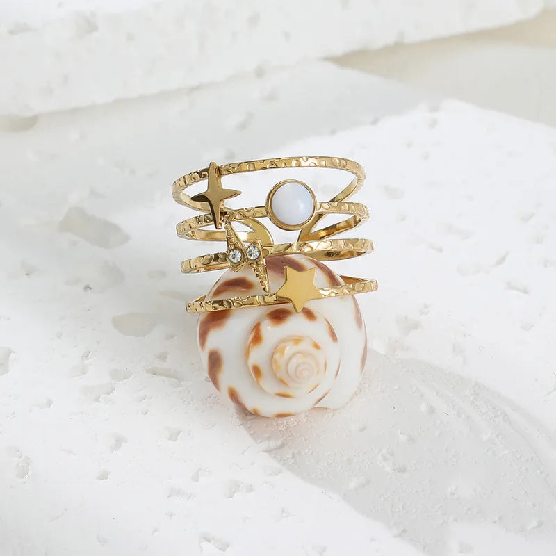 Ajoutez une touche céleste à votre style avec cette bague manchette dorée au design astral. Conçue en acier inoxydable doré, cette pièce unique arbore une étoile à 4 branches, un éclair incrusté de strass, un disque nacré et une étoile filante. L’ensemble repose sur une base martelée à plusieurs anneaux, apportant une texture raffinée et une structure moderne.