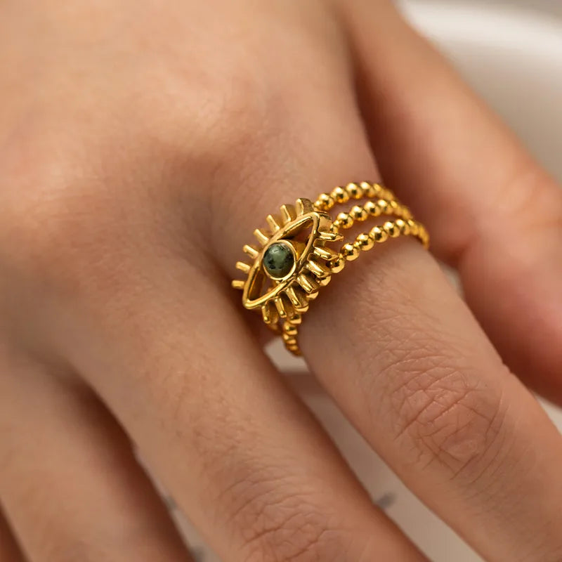 Affichez votre force intérieure avec cette bague œil dorée en acier inoxydable, au design symbolique et structuré. Son motif d’œil protecteur est rehaussé par une pierre ronde verte centrale, entourée de trois rangées de perles dorées texturées. Une pièce forte et mystique à porter au quotidien.