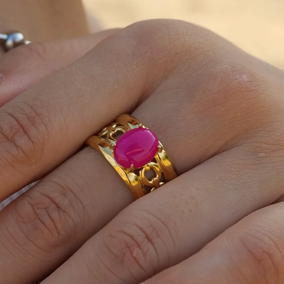 Affirmez votre style avec cette bague dorée ajourée, ornée d’un cabochon rose fuchsia éclatant. Son anneau travaillé de motifs baroques apporte relief et raffinement, tandis que la pierre centrale intensifie l’allure avec une touche glamour et assumée.