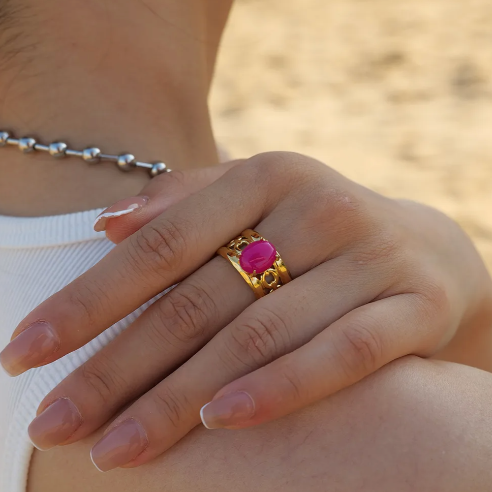 Affirmez votre style avec cette bague dorée ajourée, ornée d’un cabochon rose fuchsia éclatant. Son anneau travaillé de motifs baroques apporte relief et raffinement, tandis que la pierre centrale intensifie l’allure avec une touche glamour et assumée.
