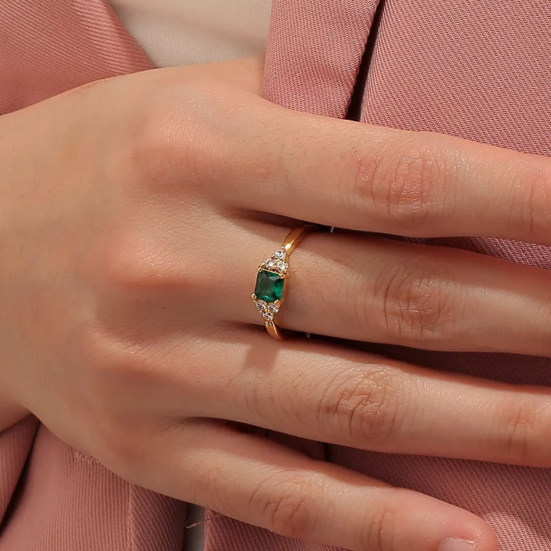 Bague plaqué or avec pierre verte taille émeraude encadrée de zircons blancs, au design symétrique et raffiné rappelant la joaillerie de prestige.
