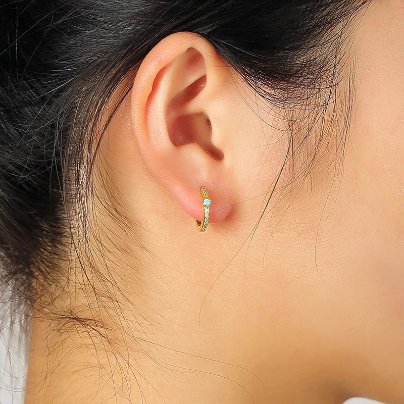 Boucles d’oreilles créoles dorées pour femme en plaqué or, serties d’une opale ronde irisée et de zircons scintillants. Bijou féminin et raffiné au design épuré, alliant éclat et mystère, parfait pour un style bohème chic et lumineux