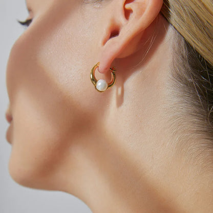 Boucles d’oreilles créoles dorées pour femme en plaqué or, ornées d’une perle blanche suspendue au centre de l’anneau. Bijou chic et féminin au style classique et contemporain, lumineux et raffiné, parfait pour une tenue élégante ou de soirée.