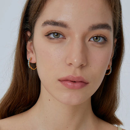 Boucles d’oreilles créoles dorées pour femme en plaqué or, ornées de pierres turquoise rondes et de détails perlés sertis. Bijou lumineux et estival au style bohème chic, parfait pour illuminer une tenue du quotidien ou une escapade en bord de mer.