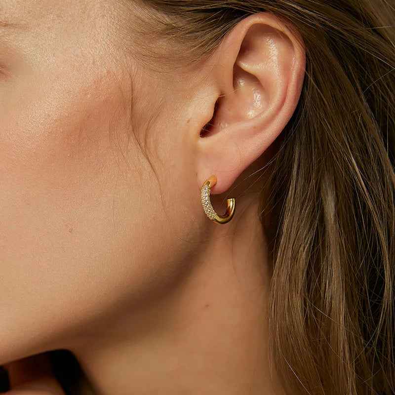 Boucles d’oreilles créoles dorées pour femme en plaqué or, serties de zircons blancs ronds sur la face extérieure. Bijou chic et minimaliste au design semi-ouvert, raffiné et lumineux, idéal pour un look élégant au quotidien ou en soirée