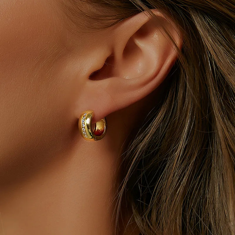 Boucles d’oreilles créoles dorées épaisses pour femme en plaqué or, ornées d’une ligne verticale de zircons scintillants incrustés au centre. Bijou contemporain chic au design épuré et lumineux, idéal pour un style élégant et professionnel au quotidien