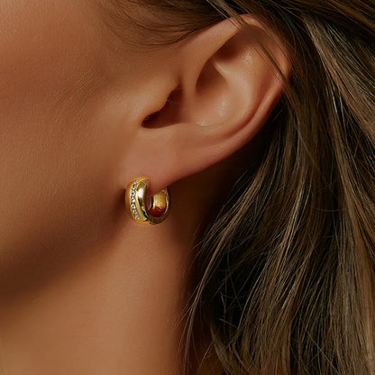 Boucles d’oreilles créoles dorées épaisses pour femme en plaqué or, ornées d’une ligne verticale de zircons scintillants incrustés au centre. Bijou contemporain chic au design épuré et lumineux, idéal pour un style élégant et professionnel au quotidien