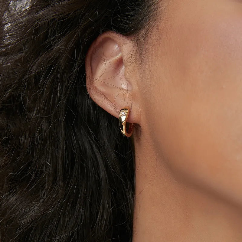 Boucles d’oreilles créoles dorées pour femme en plaqué or, inspirées de la symbolique céleste avec un zircon serti en étoile du nord à huit branches. Bijou élégant et lumineux au poli miroir, léger et raffiné, parfait pour un style solaire et minimaliste