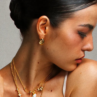 Boucles d’oreilles dorées en acier inoxydable pour femme, au design spirale coquillage, finitions brillantes, style moderne et raffiné.