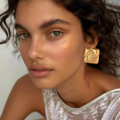 Paire de boucles d’oreilles dorées carrées en acier inoxydable, au design spiralé brillant et à l’effet miroir, parfaites pour un look chic et contemporain.